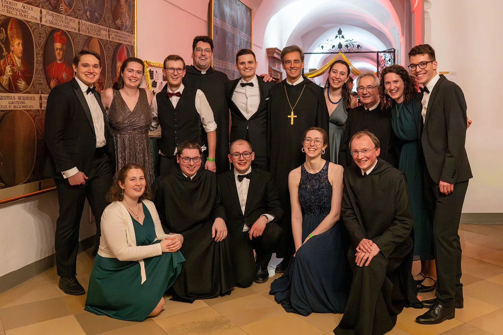 Gruppe von Menschen in formeller Kleidung, einige in Talar, bei einer Feier in einem historischen Gebäude mit Wandgemälden