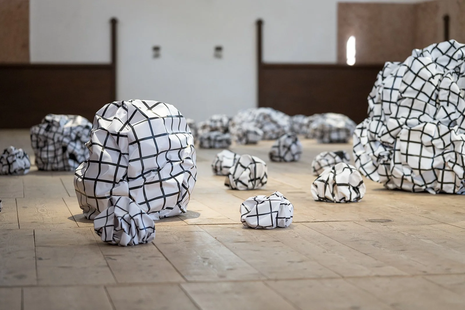 Mehrere zerknüllte Papierbälle mit schwarzem Gittermuster auf Holzboden in einem Raum.