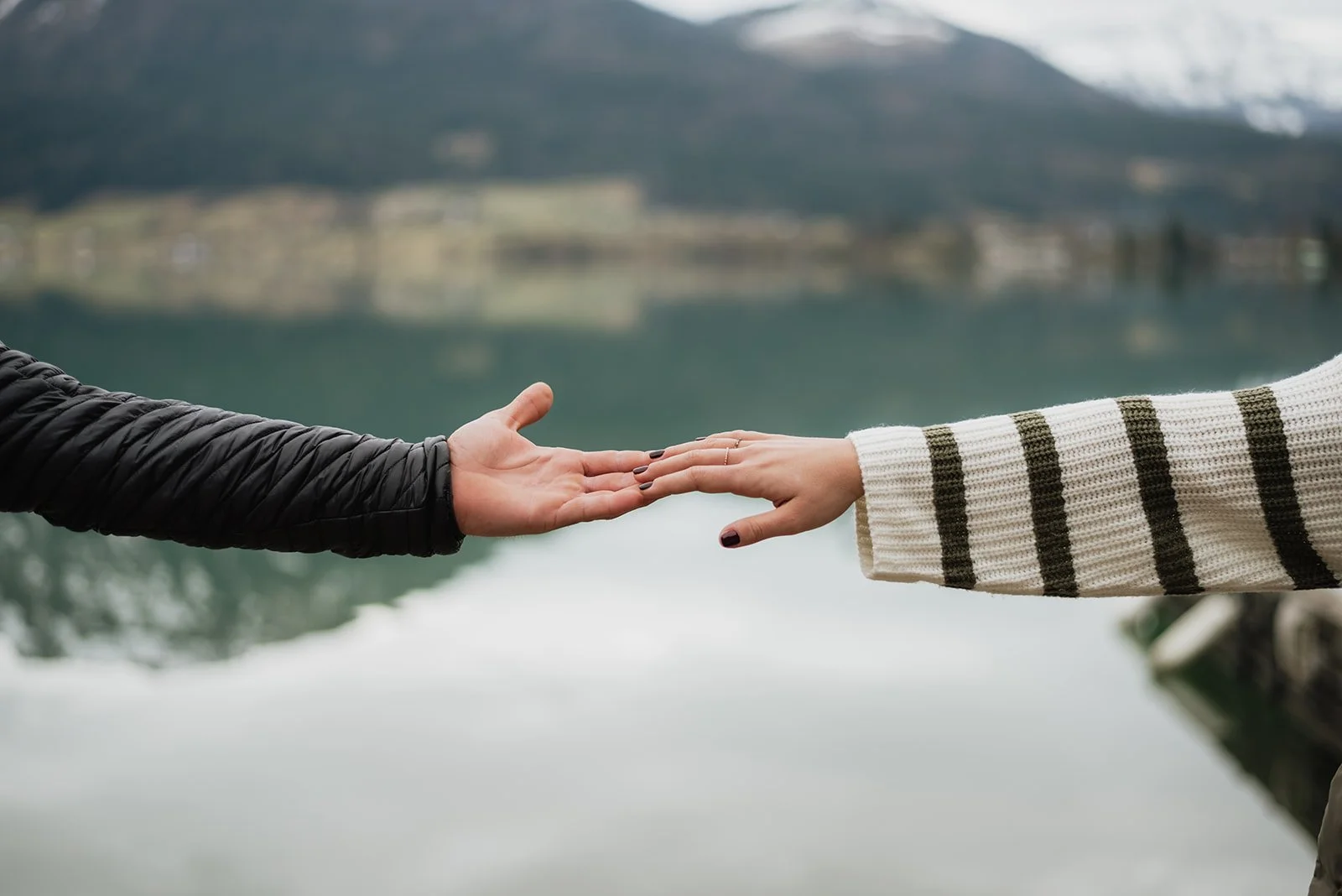 Zwei Menschen stoßen ihre Hände auf einem See mit Bergen im Hintergrund an.