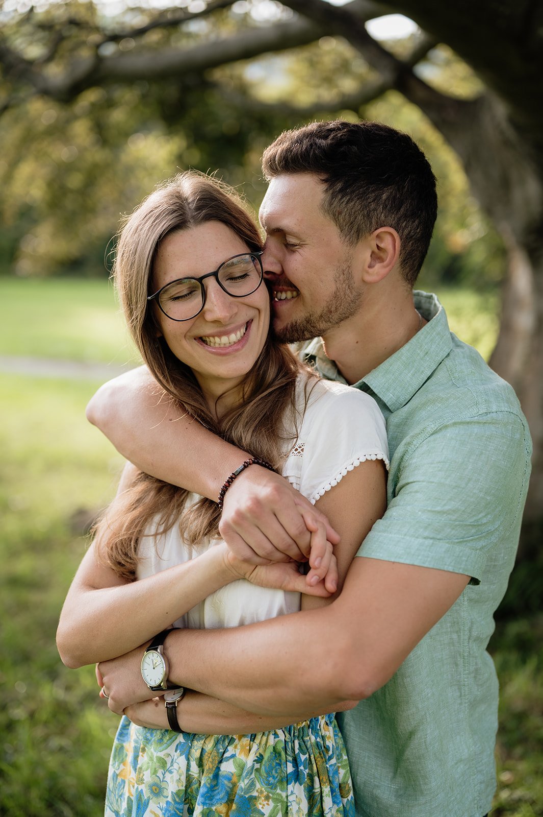 Ein glückliches Paar umarmt sich in einem Park, mit Bäumen im Hintergrund.