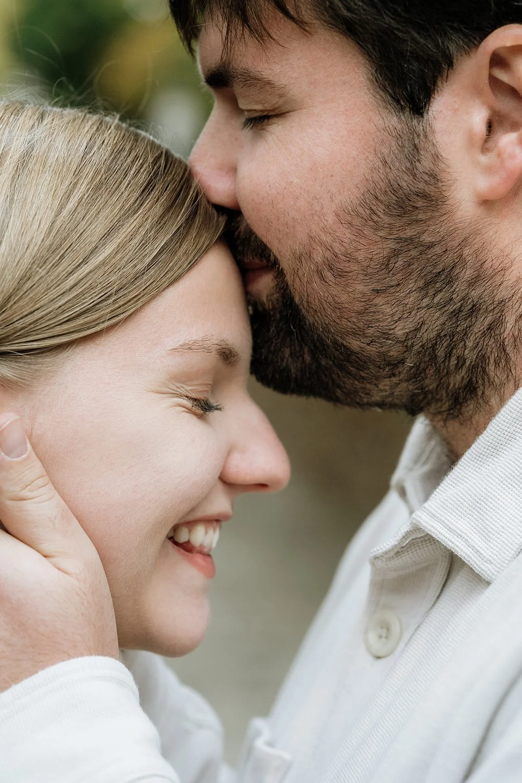 Ein Mann und eine Frau teilen einen liebevollen Moment, wobei der Mann den Kopf der Frau sanft an seine Stirn legt, beide lächeln und geschlossen die Augen haben.