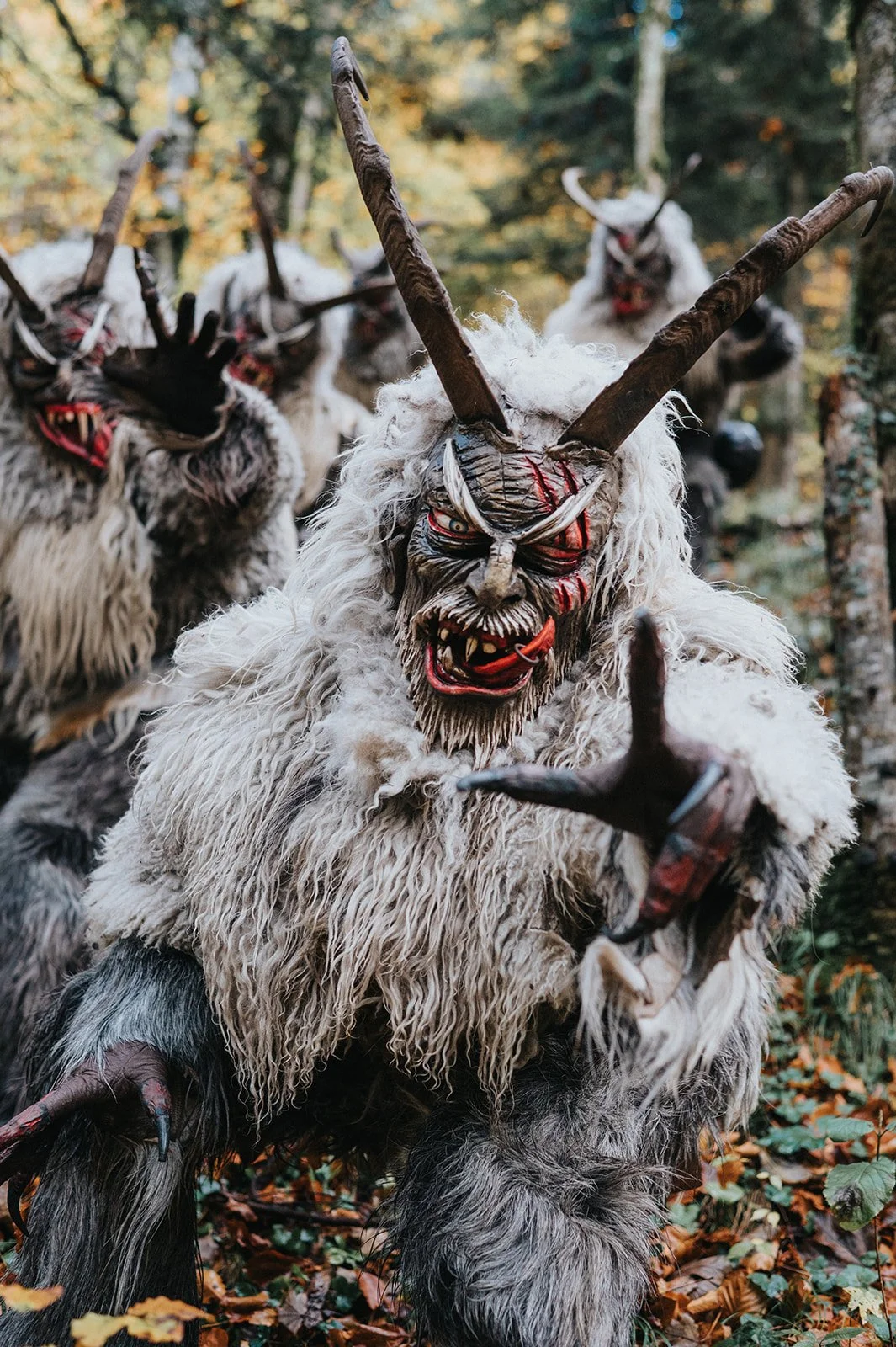 Gruppen von masksierten Figuren in Wald mit traditionellen Kostümen und Masken, die Dämonen darstellen.
