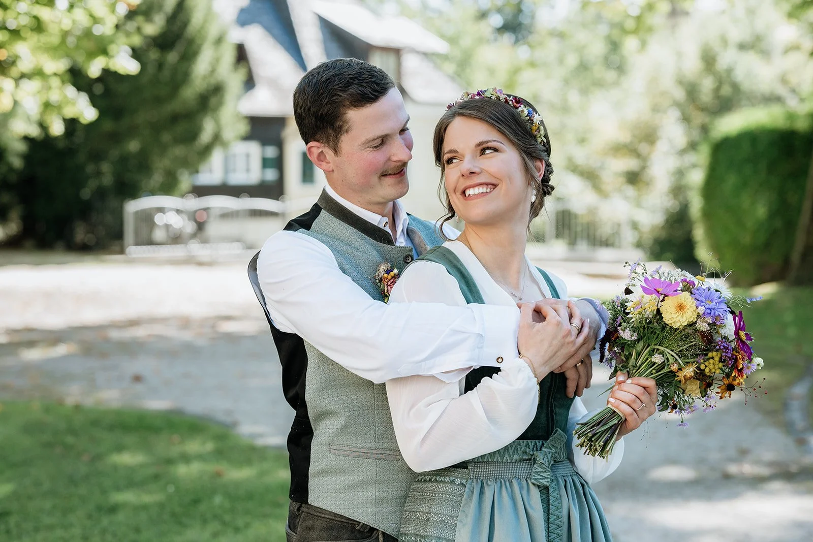 Romantisches Brautpaar in Tracht blickt sich zueinander an. Im Hintergrund Bäume und Sträucher.