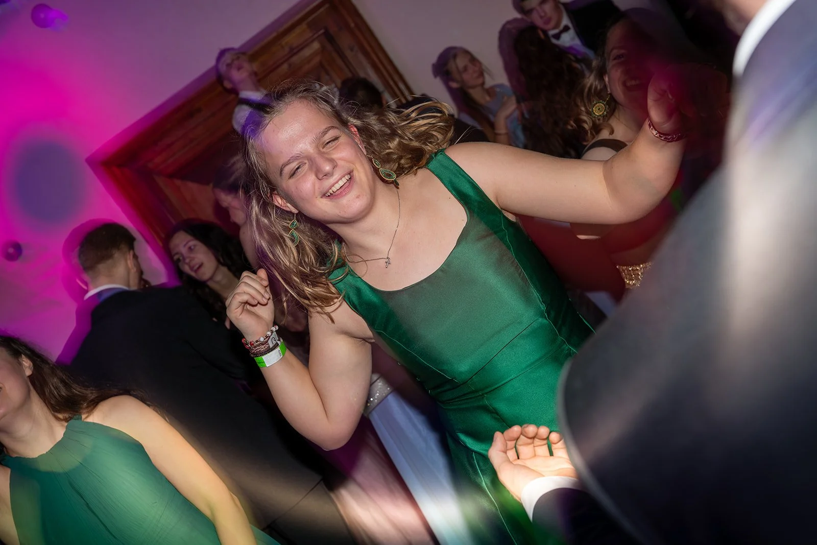 Fröhliche junge Frauen tanzen und feiern auf einer Party in einem Raum mit buntem Licht.