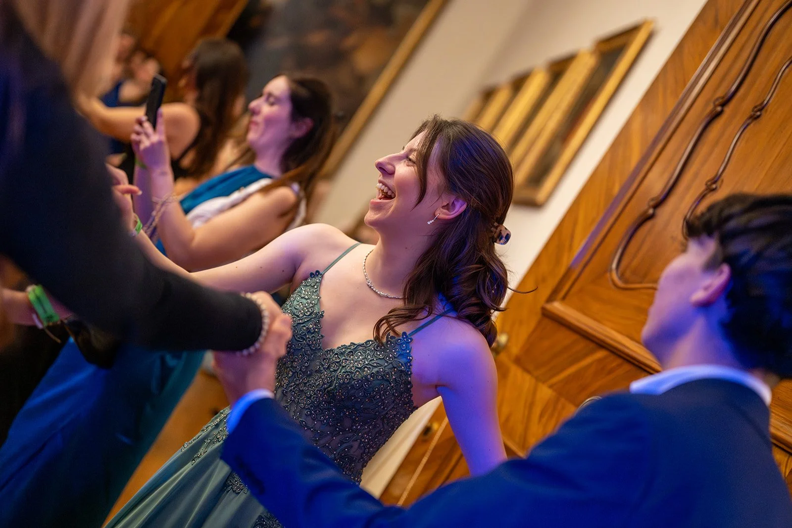 Eine Gruppe junger Menschen auf einer Party, die tanzen und lachen, im Hintergrund Holzwände und Bilder an der Wand.