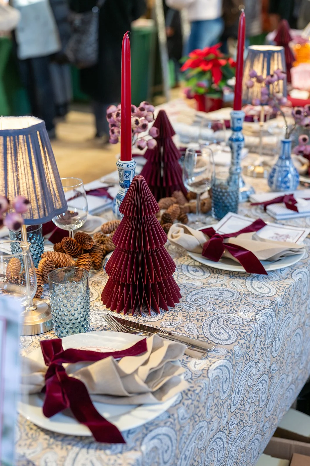 Festlich gedeckter Tisch mit Weihnachtsdekoration, including rote Kerzen, Papier-Weihnachtsbäume, Kristallgläser, und servierten Platten und Besteck.