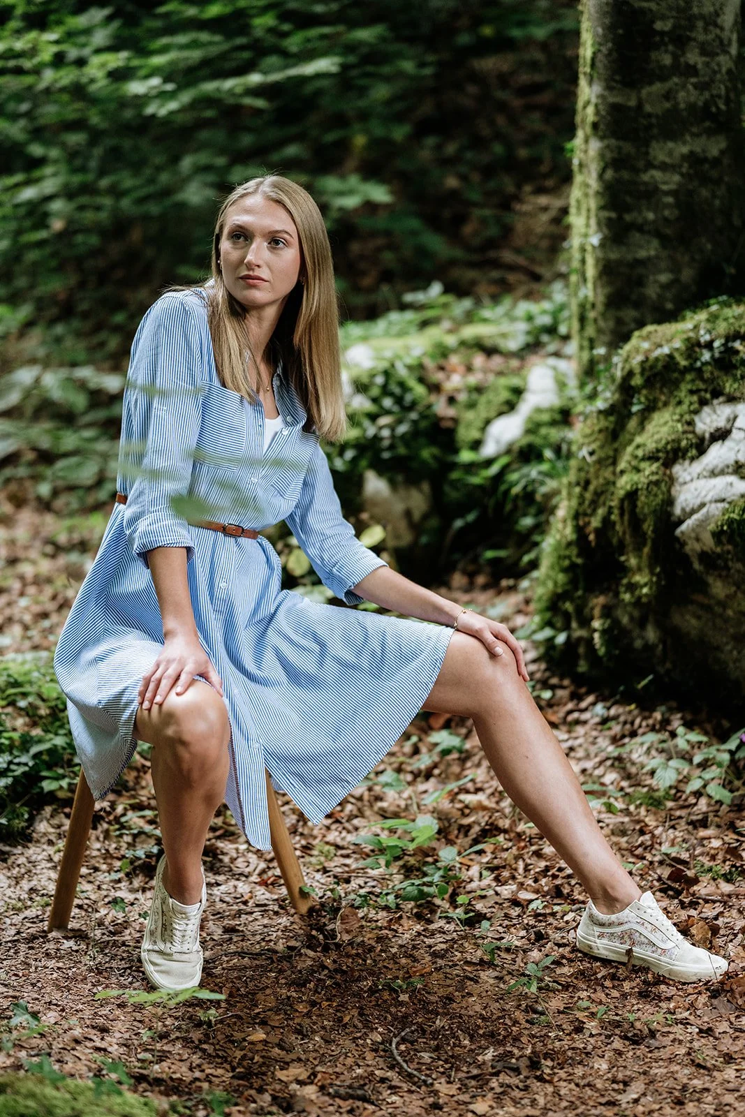 Junge Frau in Kleid in einem Wald sitzend auf einem Stuhl.