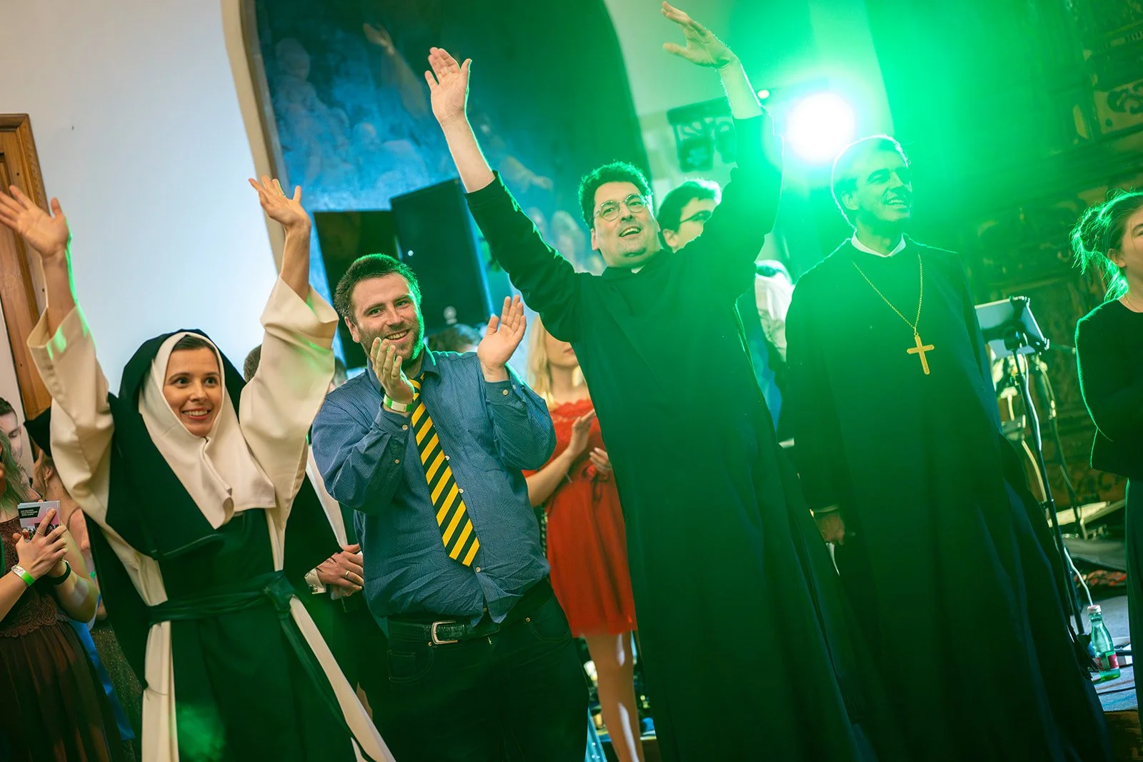 Menschen beim Fest, einige in religiöser Kleidung, feiern und jubeln, einige klatschen, im Hintergrund ein grünes Licht.