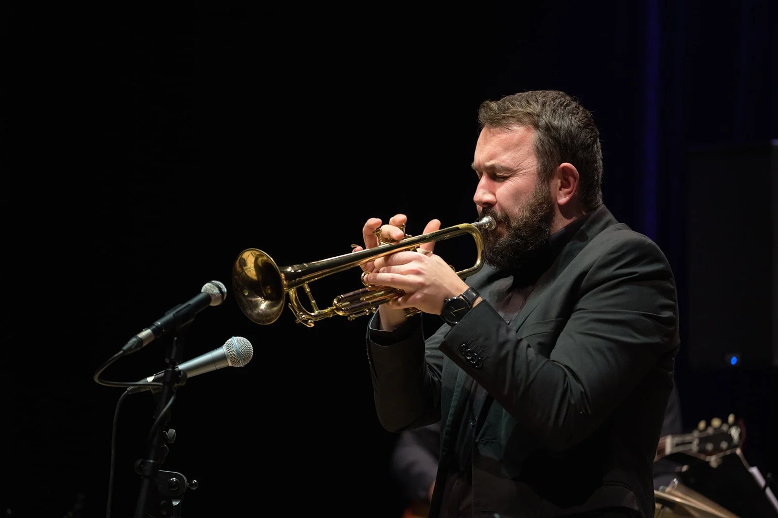 Musiker spielt Trompete auf Bühne, dunkler Hintergrund