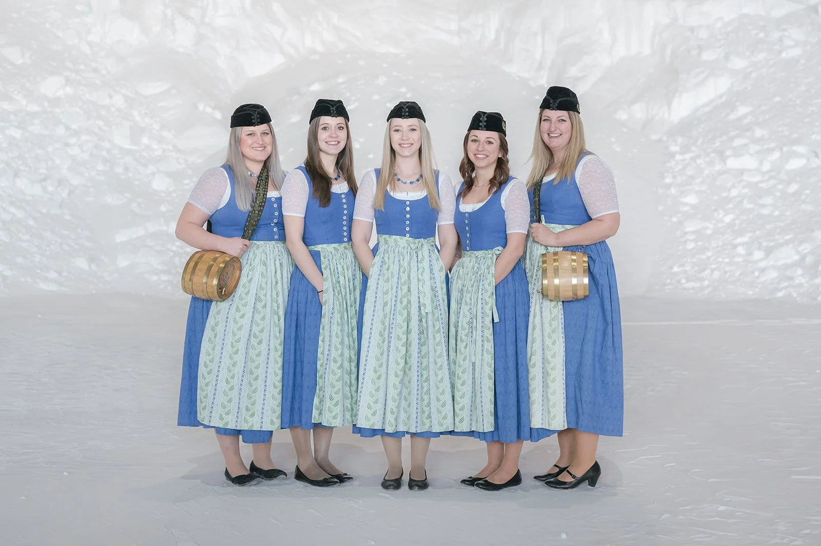 Fünf Frauen in traditionellen bayerischen Dirndls vor winterlicher Schneelandschaft.