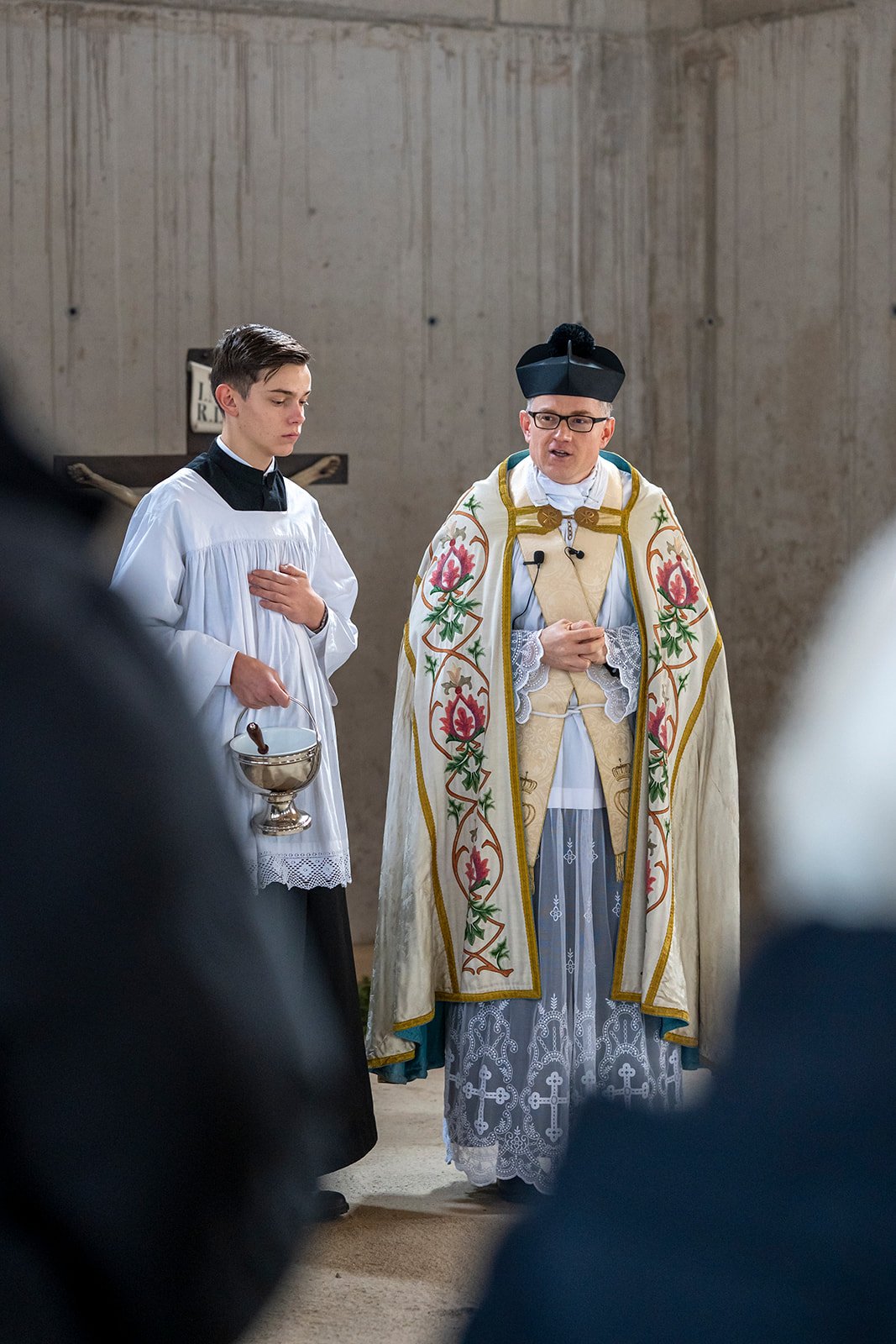 Katholischer Priester in festlicher liturgischer Kleidung, umgeben von Gläubigen, während einer Messe in einer Kirche.