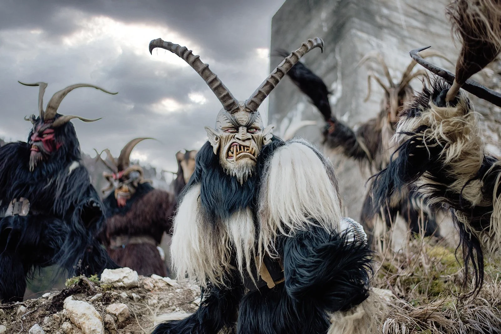 Traditionelle maschinerieartige Figuren mit Tiermasken und Hörnern bei einem Fest, die auf einem felsigen Feld im Freien stehen.