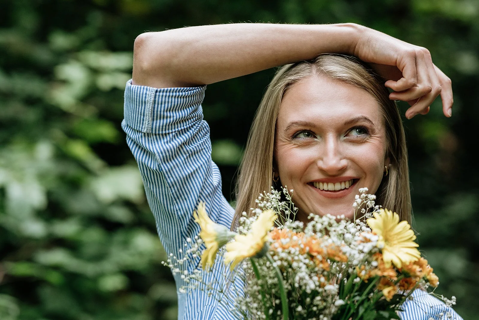 Natürliches Portraitshooting in Bad Ischl – junge Frau lächelt an der Kamera vorbei und hält einen bunten Blumenstrauß in der Hand.