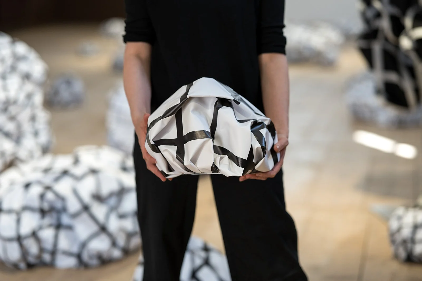 Person hält ein verpacktes Objekt mit schwarzem und weißem Muster, im Hintergrund viele weitere verpackte Gegenstände.