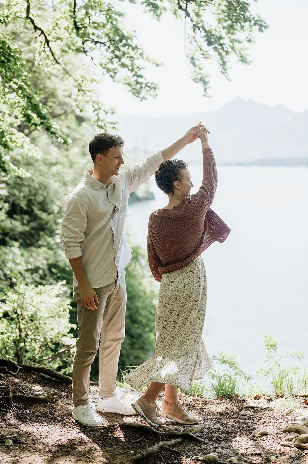 Ein Mann und eine Frau tanzen Händchen haltend an einem Fluss im Grünen an einem sonnigen Tag.