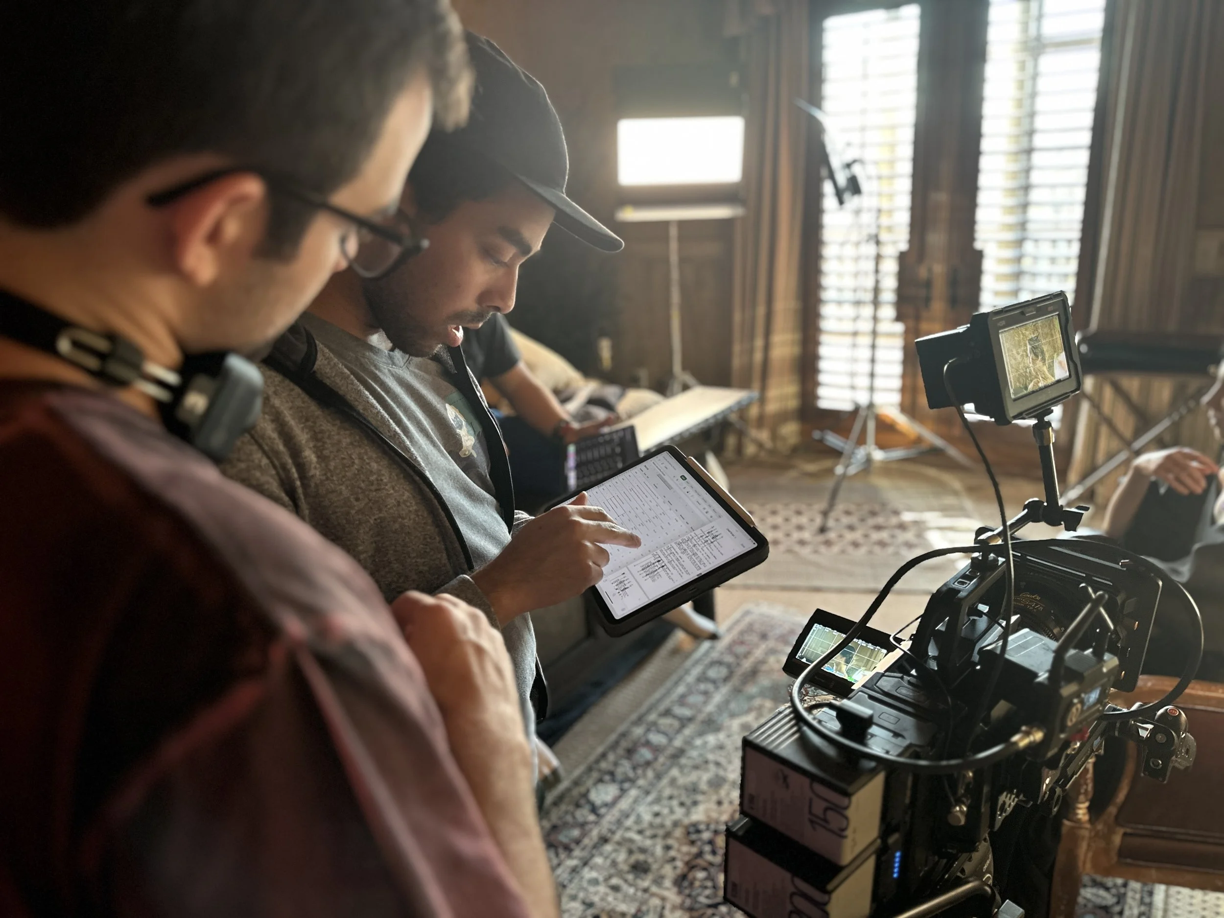 Filmmakers on set reviewing footage and coordinating, with professional camera equipment, in a room with wood walls and large windows.