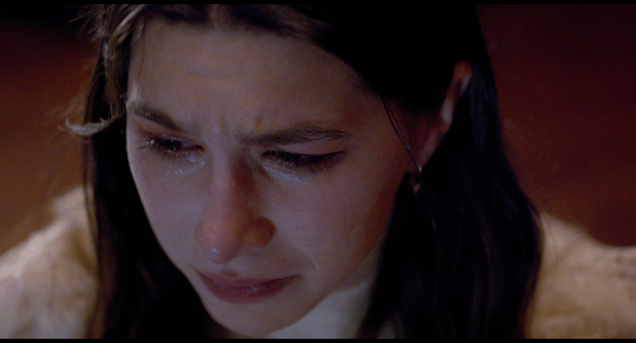 Close-up of a young woman with dark hair, looking down with a worried or sad expression.