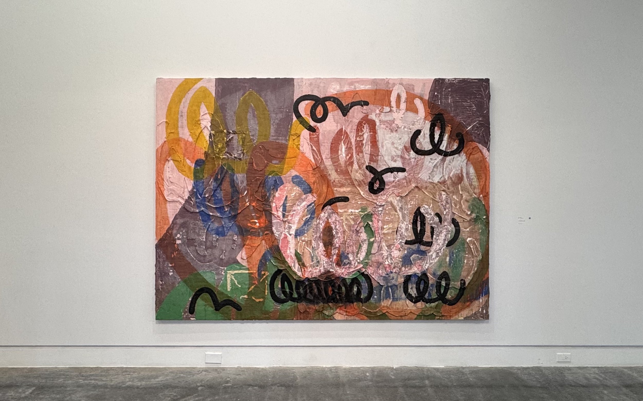 Abstract colorful painting with layered textures and black scribble-like markings on a gallery wall.