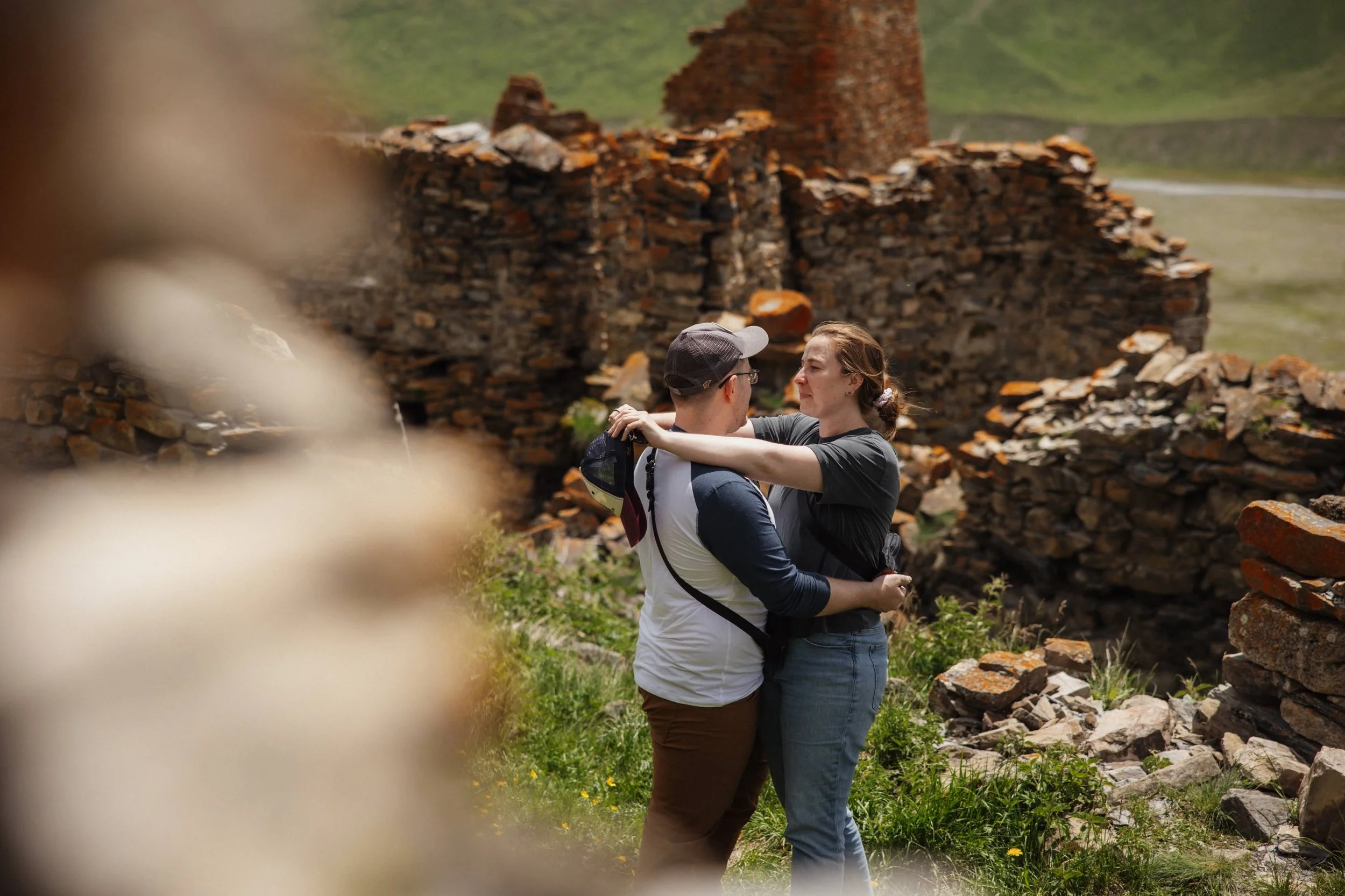 A couple dancing outdoors among the ruins of an old brick structure, with green hills in the background.