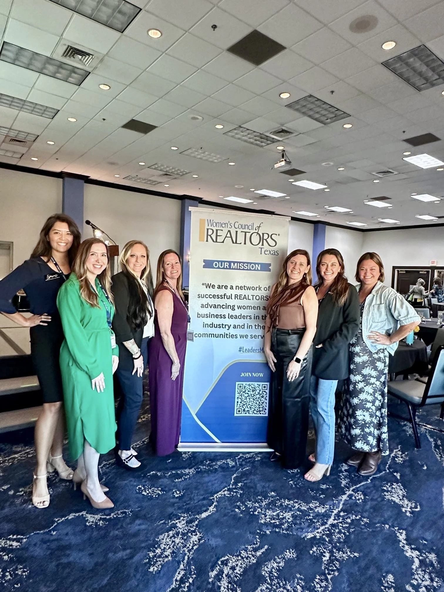Group of women standing together in front of a Women’s Council of REALTORS Texas banner at a conference or event, smiling at the camera.