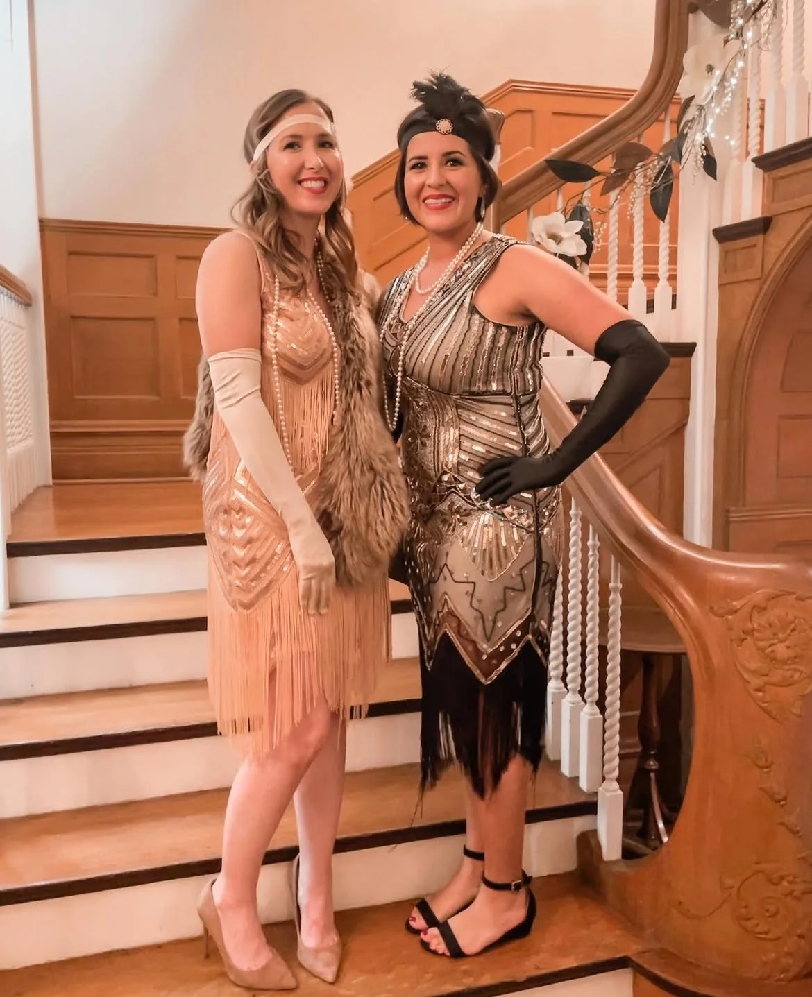 Two women in 1920s flapper dresses posing on a staircase at a costume party.