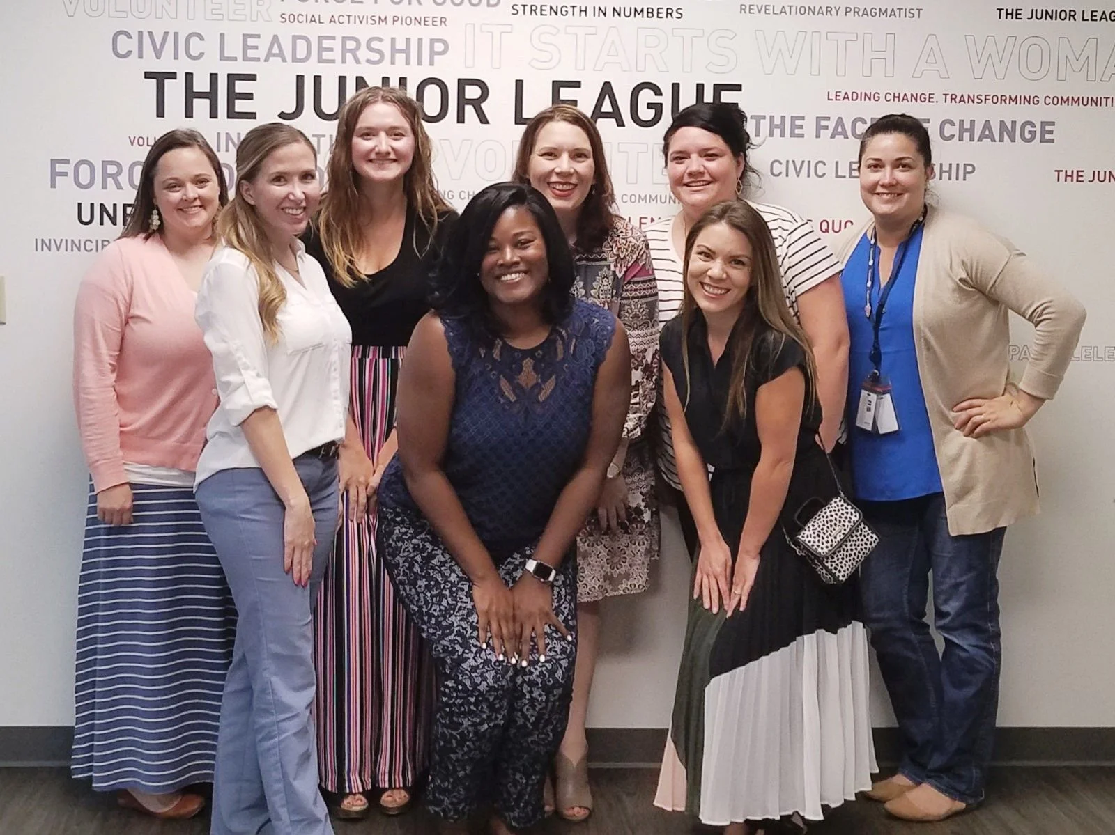 Group of nine women smiling and posing together in front of a wall with words related to leadership and activism.