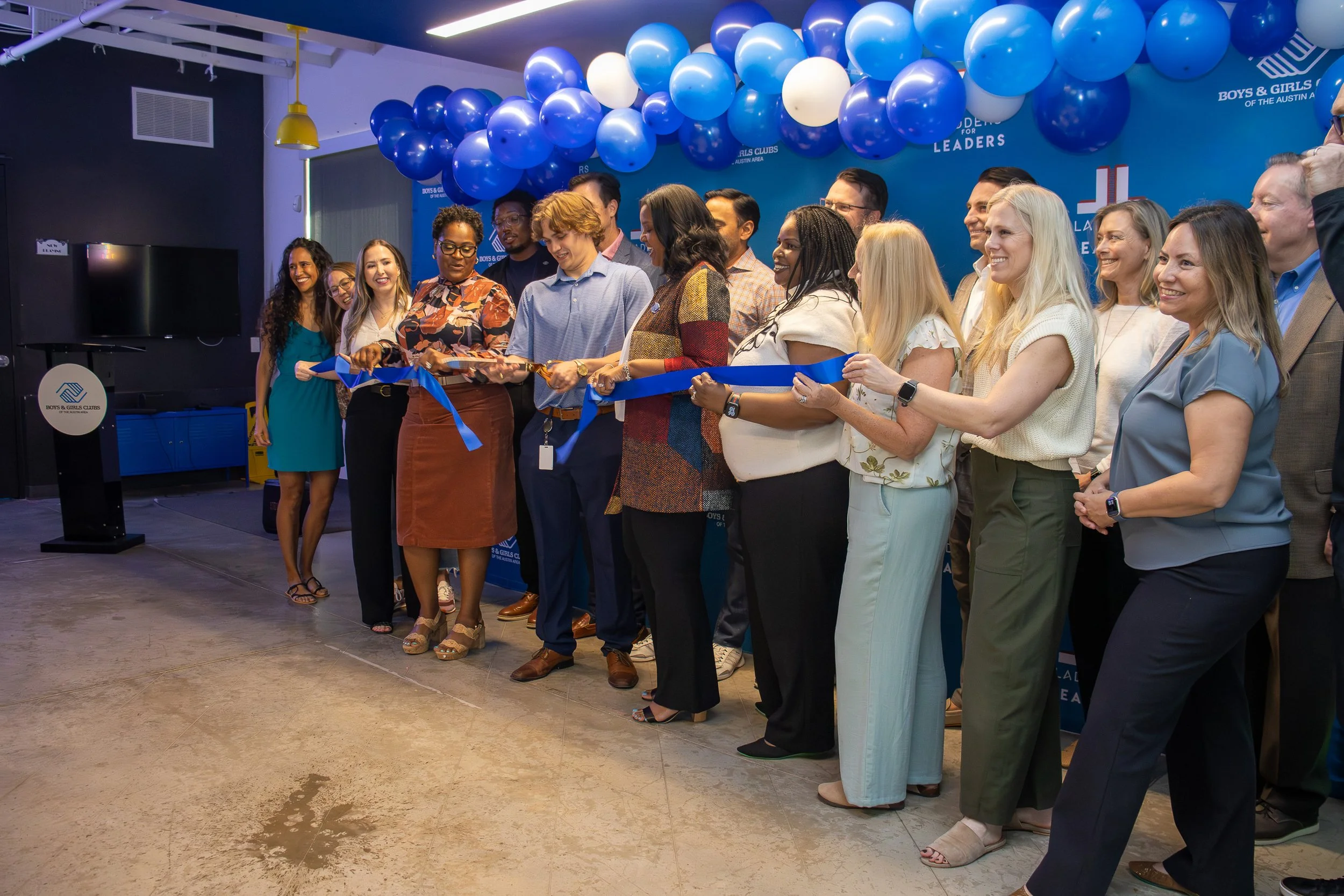 Group of diverse people participating in a ribbon-cutting ceremony at an event for Boys & Girls Clubs, with blue balloons and a blue backdrop.