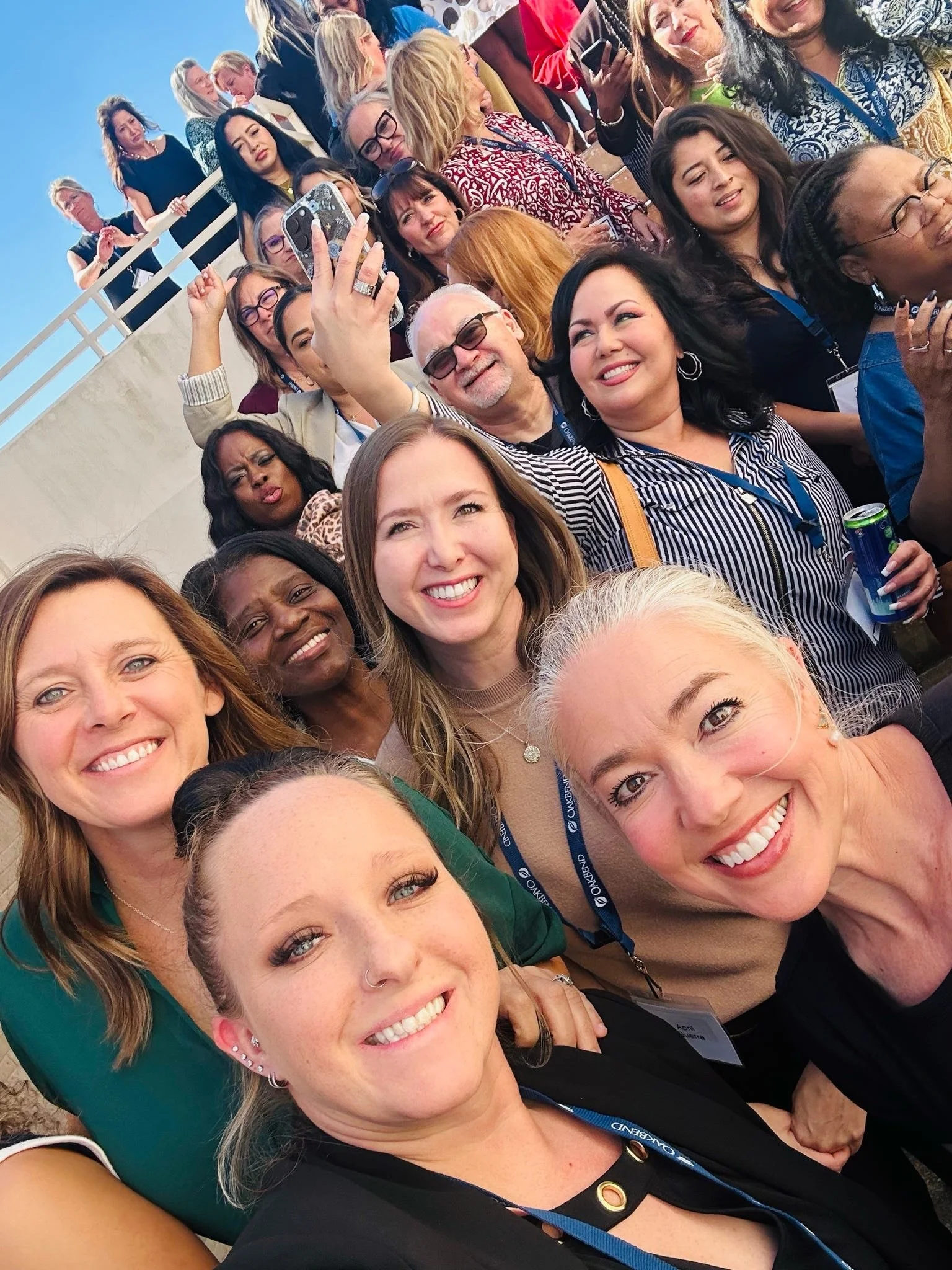 Group of diverse women and a man taking a selfie outdoors during daytime, smiling and posing for the camera.