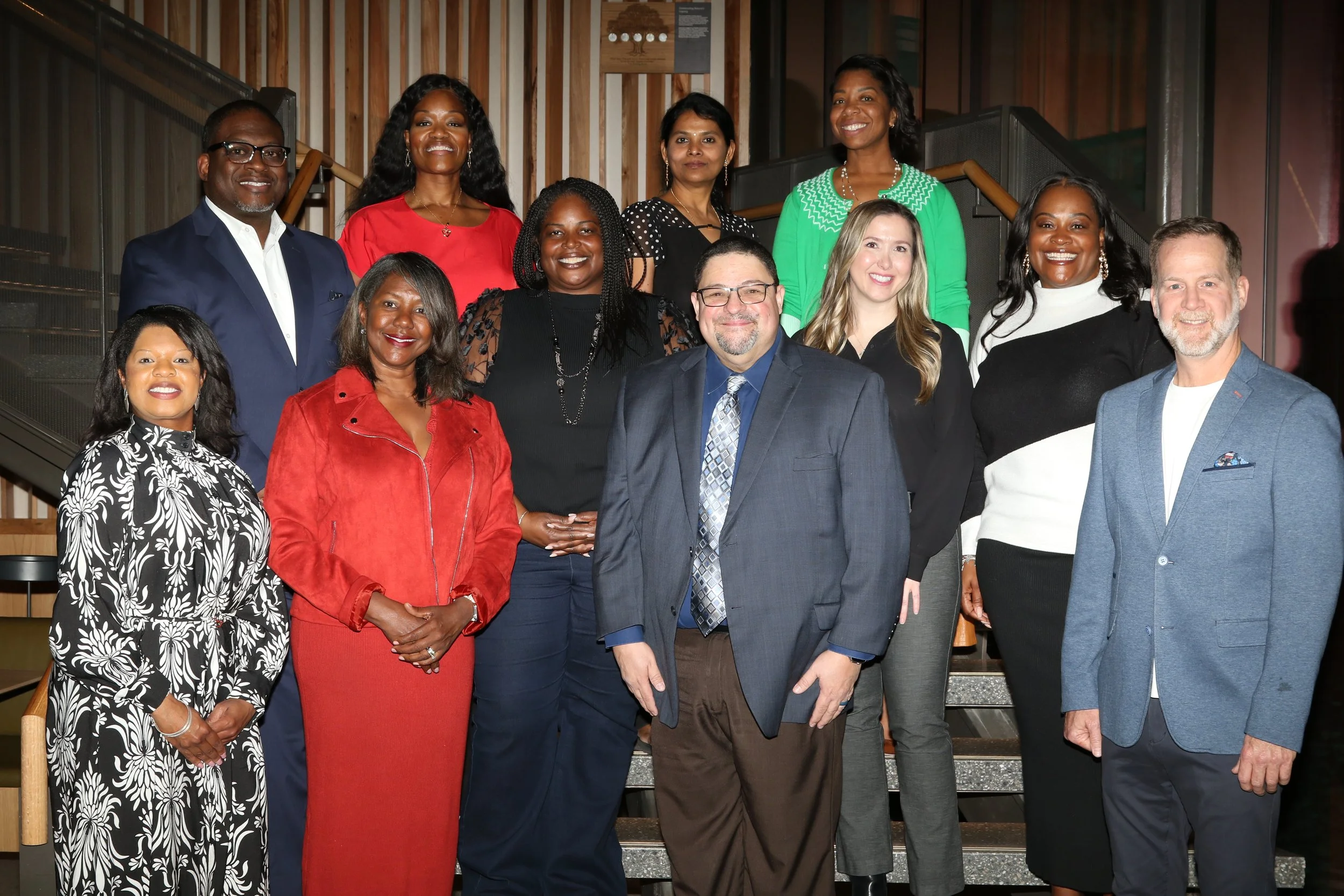 Group photo of diverse professionals dressed in business attire, standing on staircase indoors.