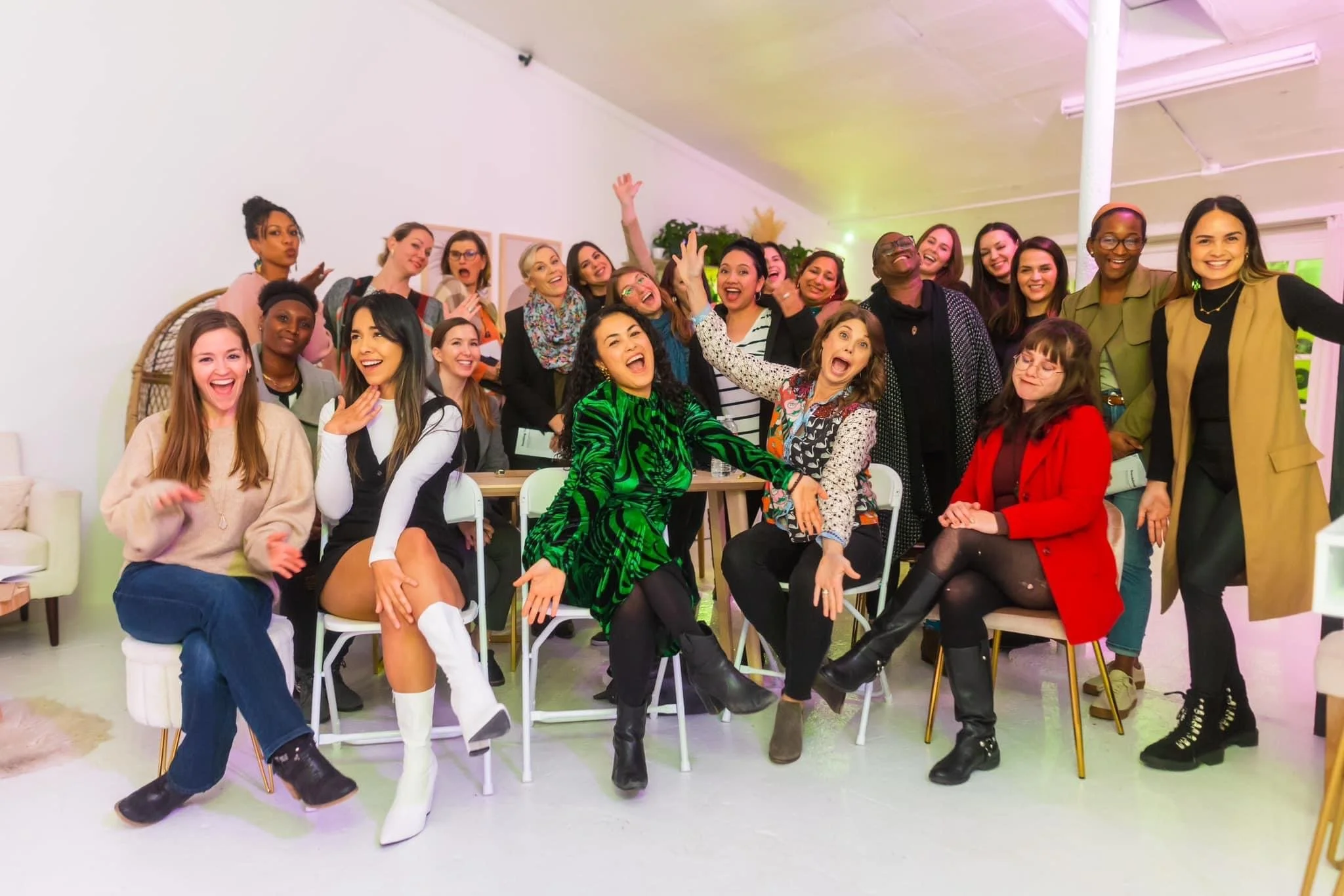 A large group of diverse women gathered together, smiling, laughing, and posing for a photo in an indoor setting with bright lighting and modern decor.