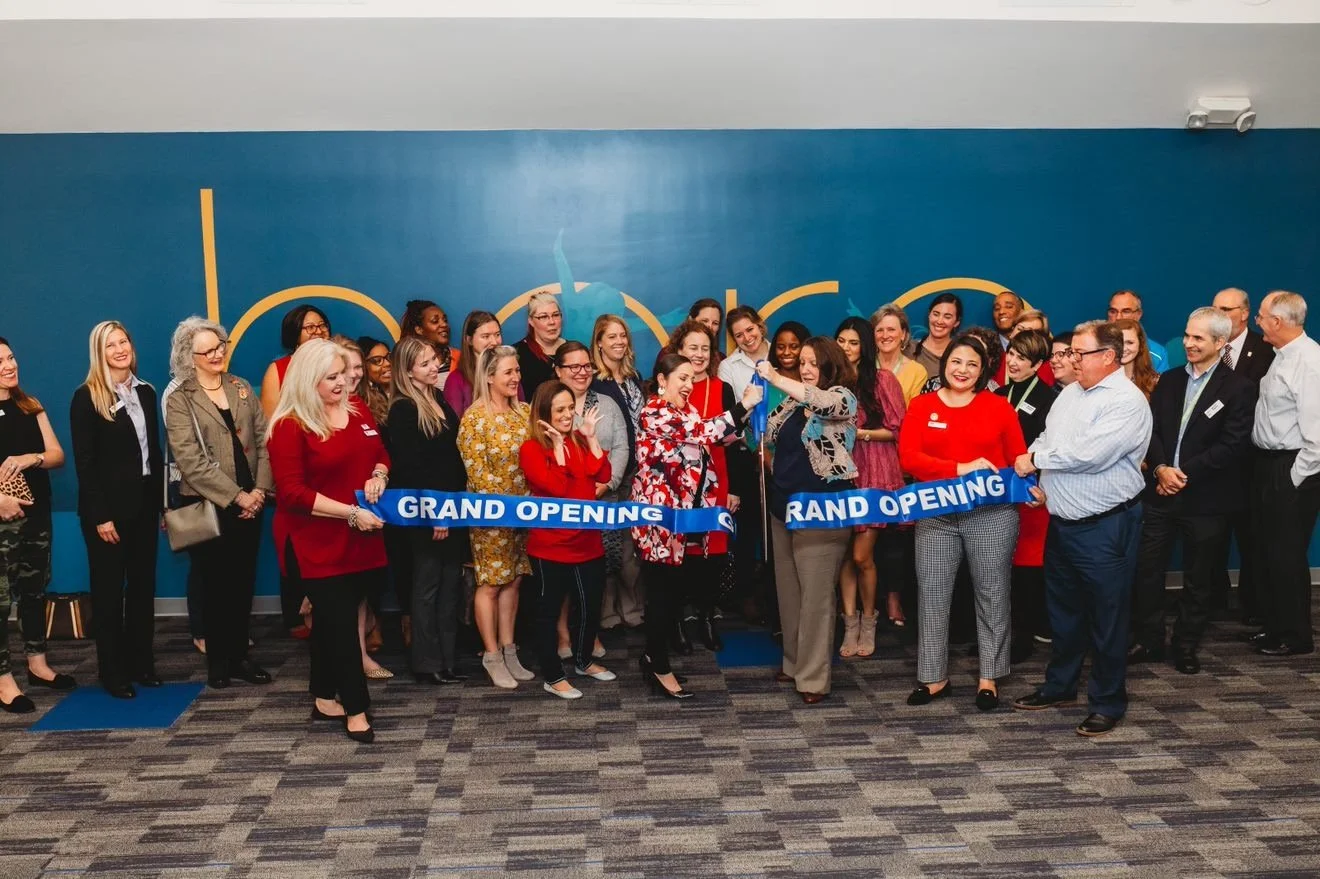 Group of diverse people celebrating grand opening with ribbon cutting in an indoor space with blue walls.