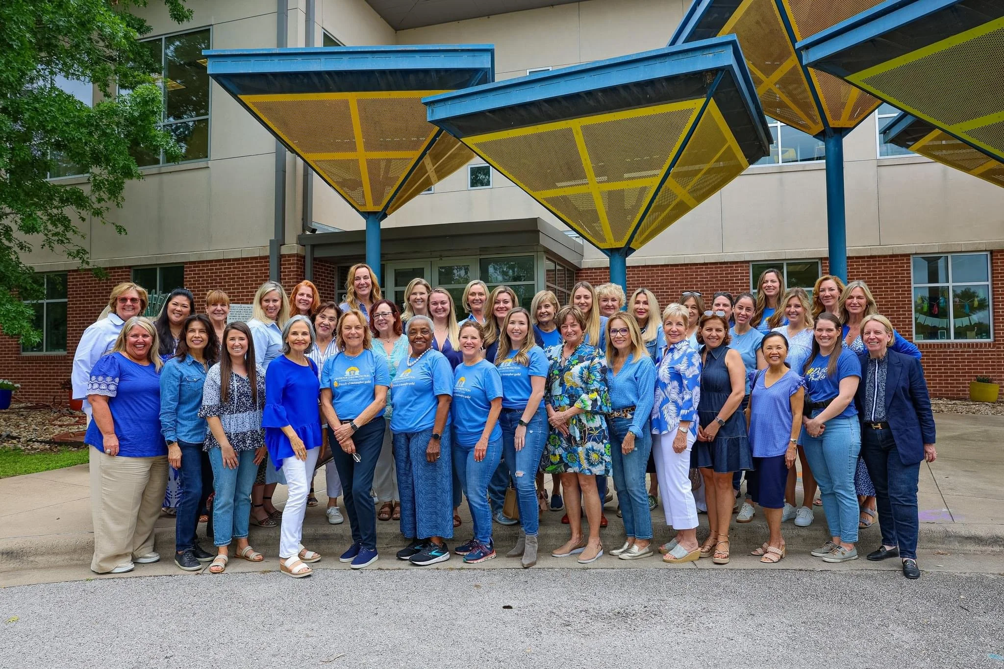 Group of diverse women standing outside a building with modern architectural features, wearing blue clothing.