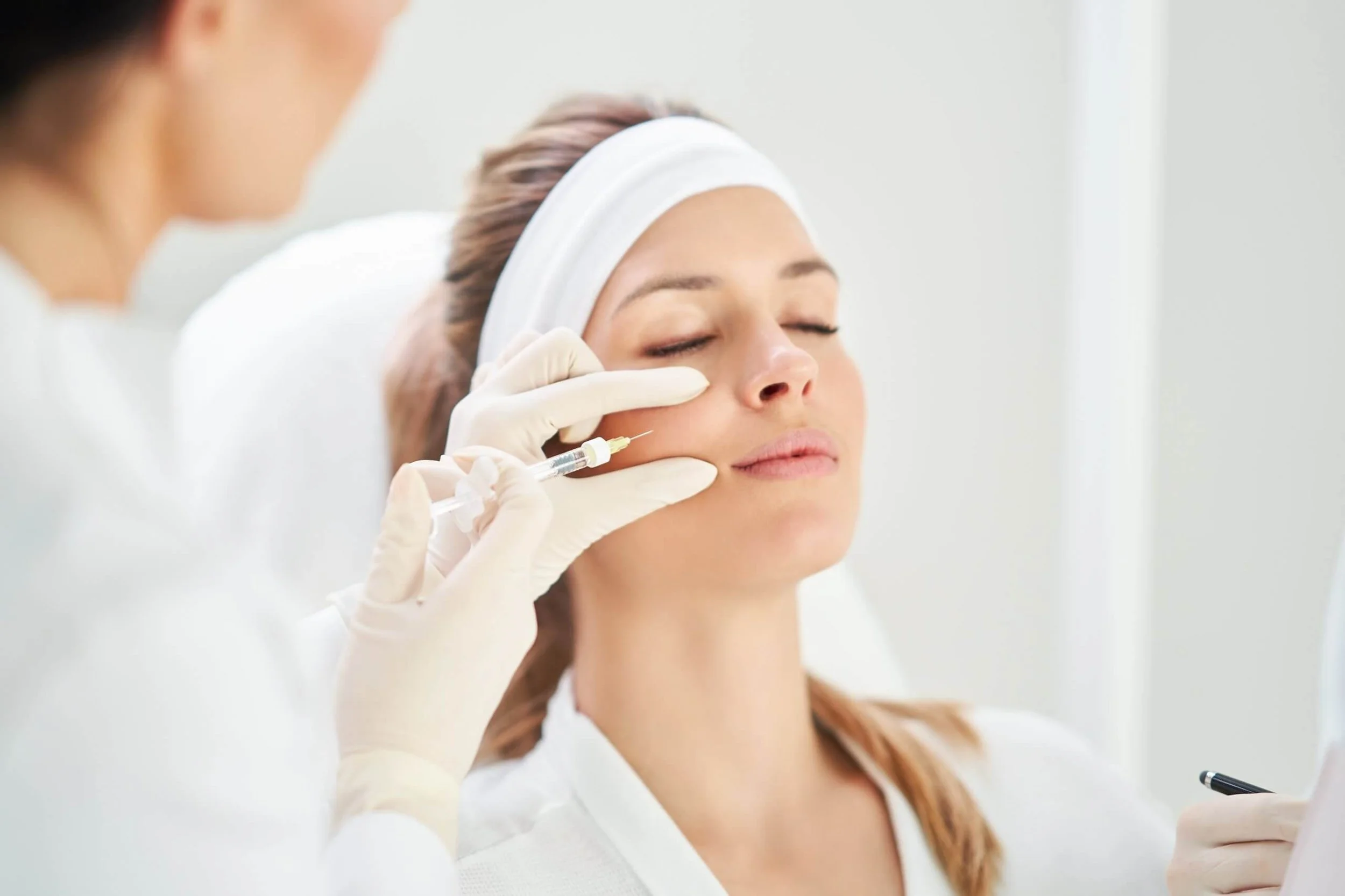 A woman receives a facial injection from a skincare specialist in a clinical setting.