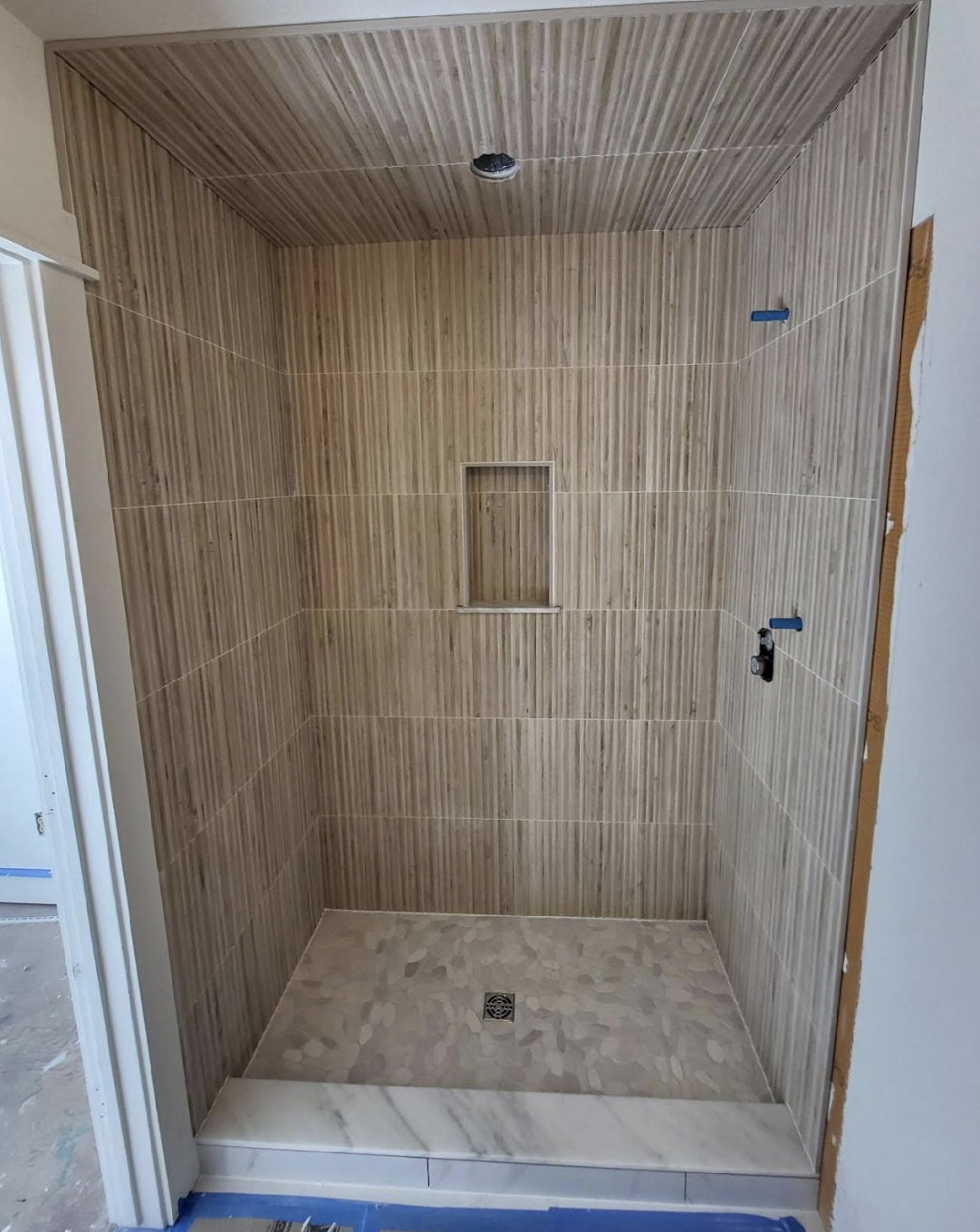Undermount shower with wood-look wall tiles, a marble threshold, and a tiled shower floor with a drain in the center.