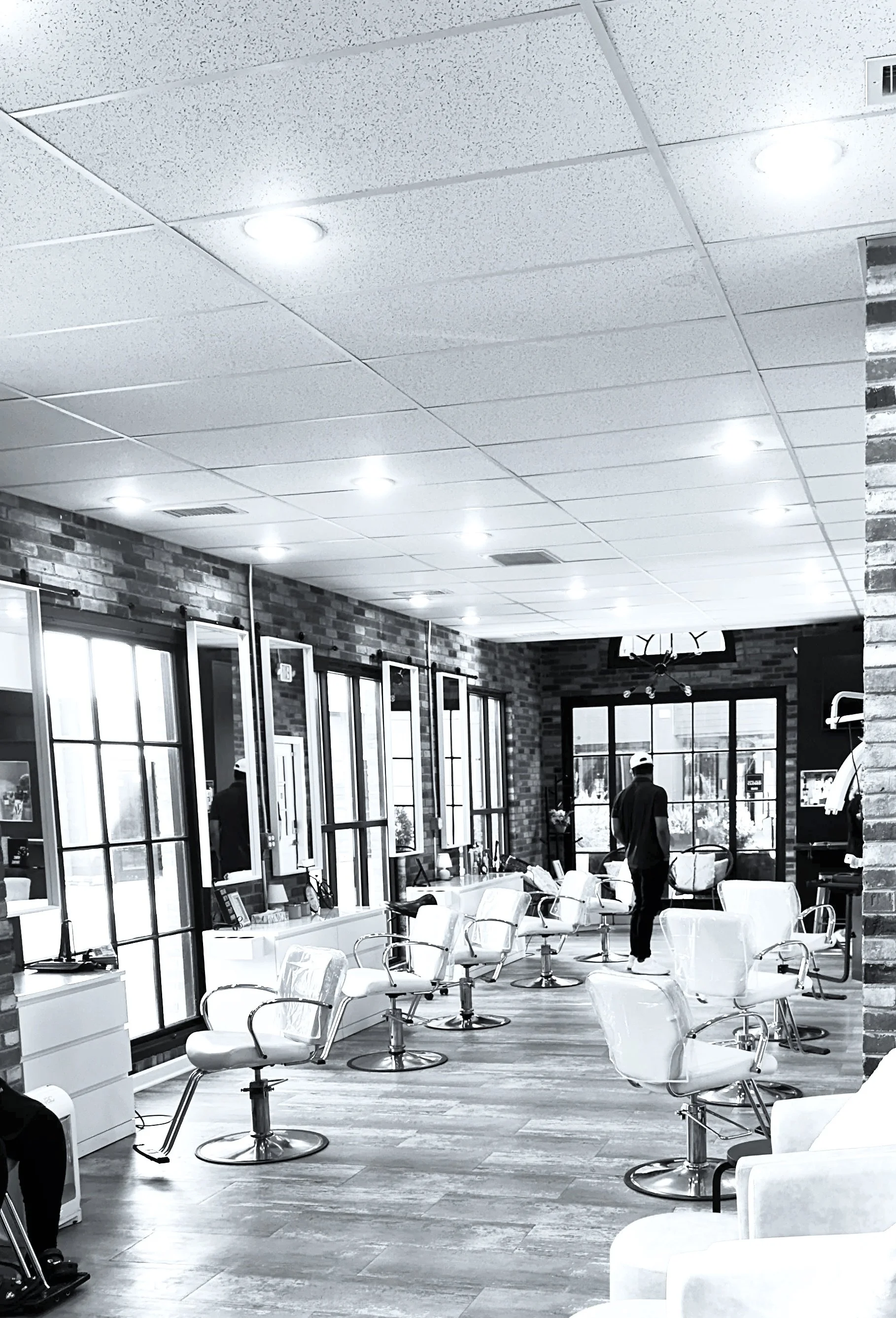 A black and white photo of a hair salon with multiple styling chairs, mirrors, and large windows