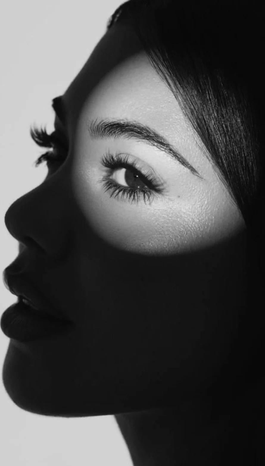Close-up black and white portrait of a woman's face, mainly showing one eye and part of her lips, with her eye gazing sideways.
