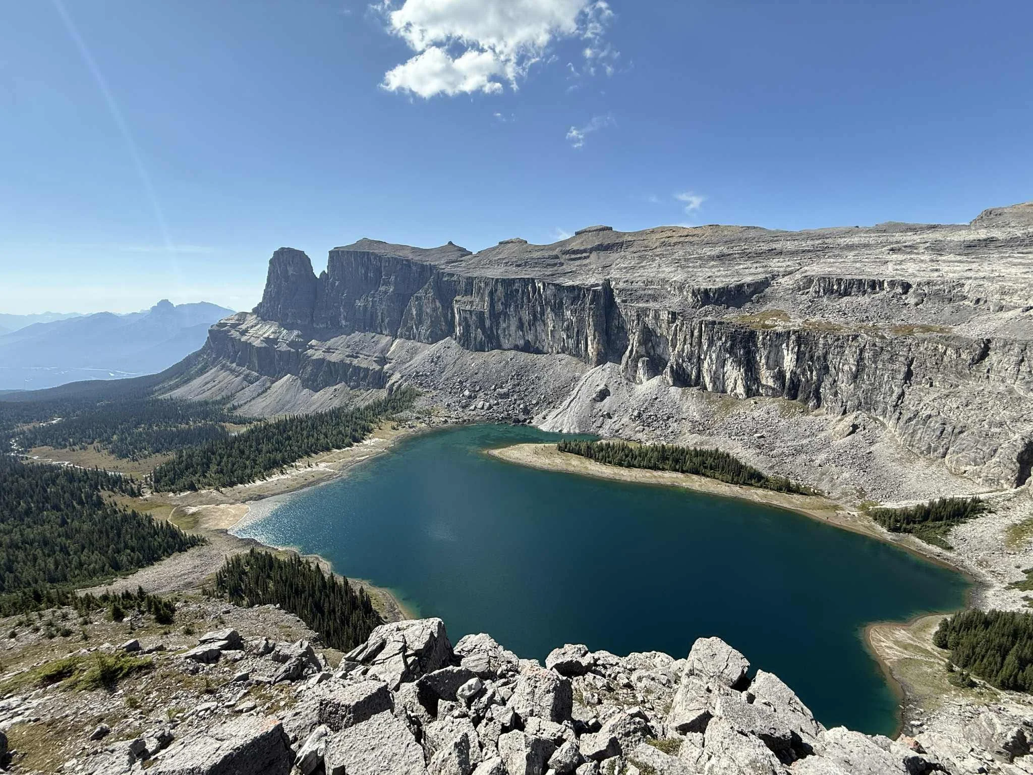 A mountain lake surrounded by rocky cliffs and dense forest under a clear blue sky.