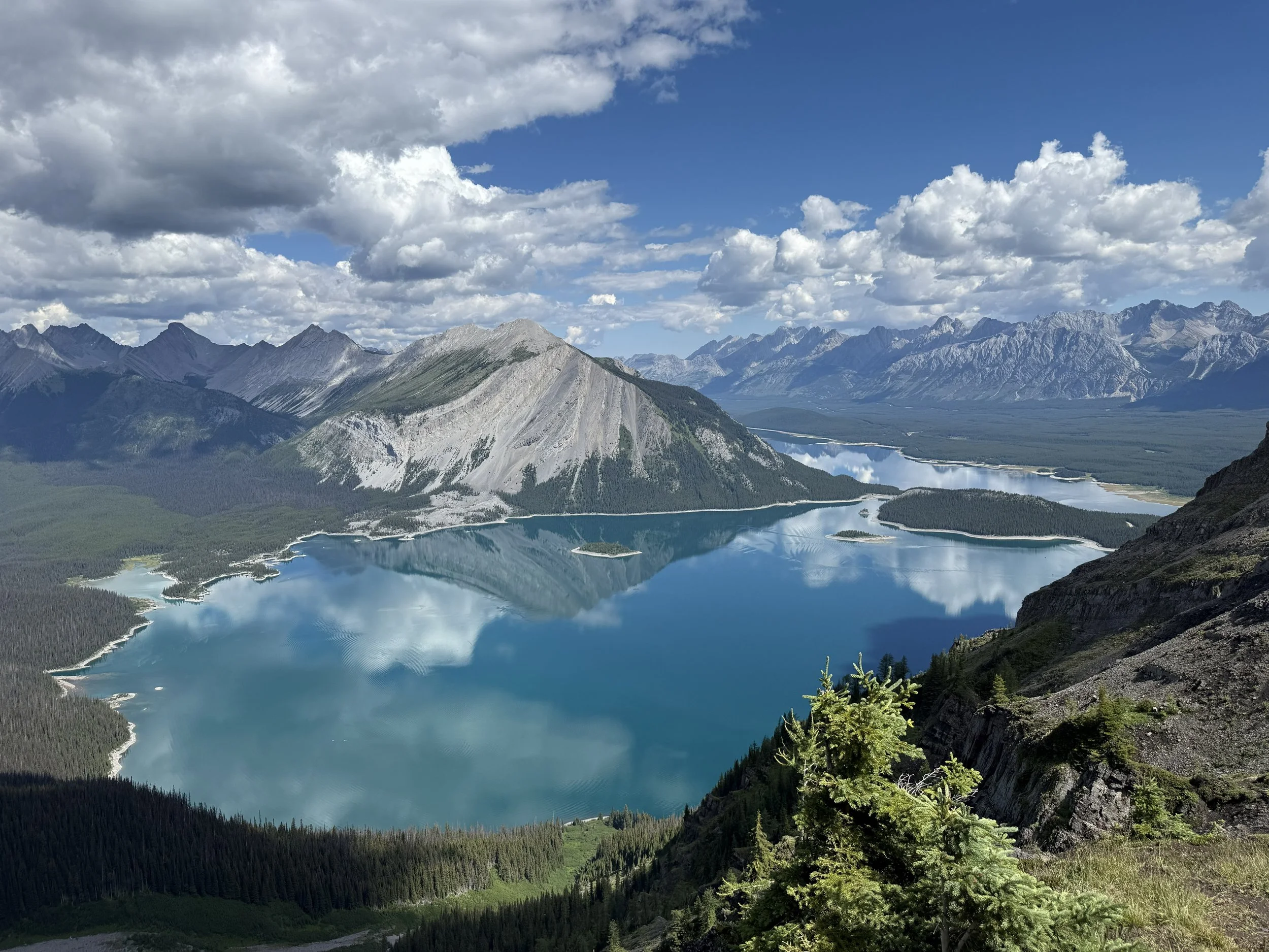 Scenic view of a mountain lake reflecting the cloudy sky, surrounded by mountains and dense forest.