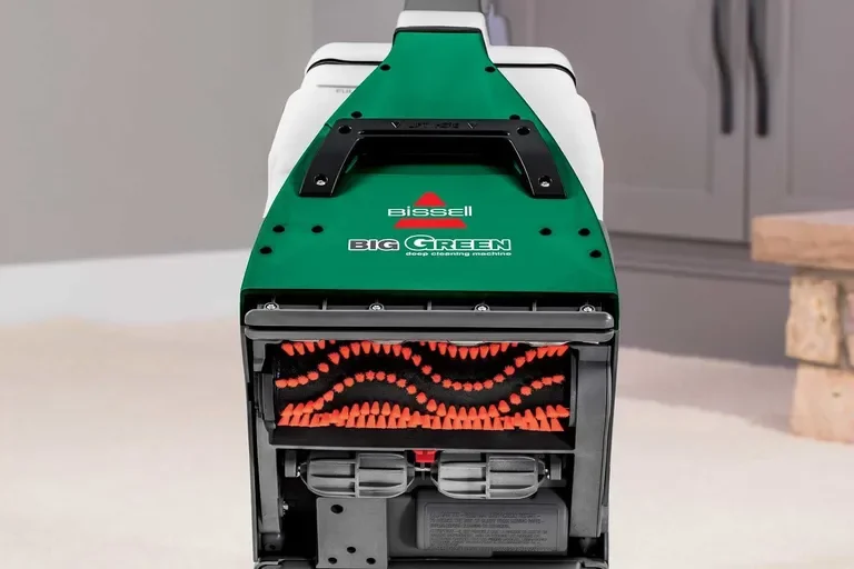 A green and black deep cleaning machine with a handle on top, labeled "BIOSSELL BIG GREEN deep cleaning machine", situated in a room with a beige carpet and a stone block in the background.