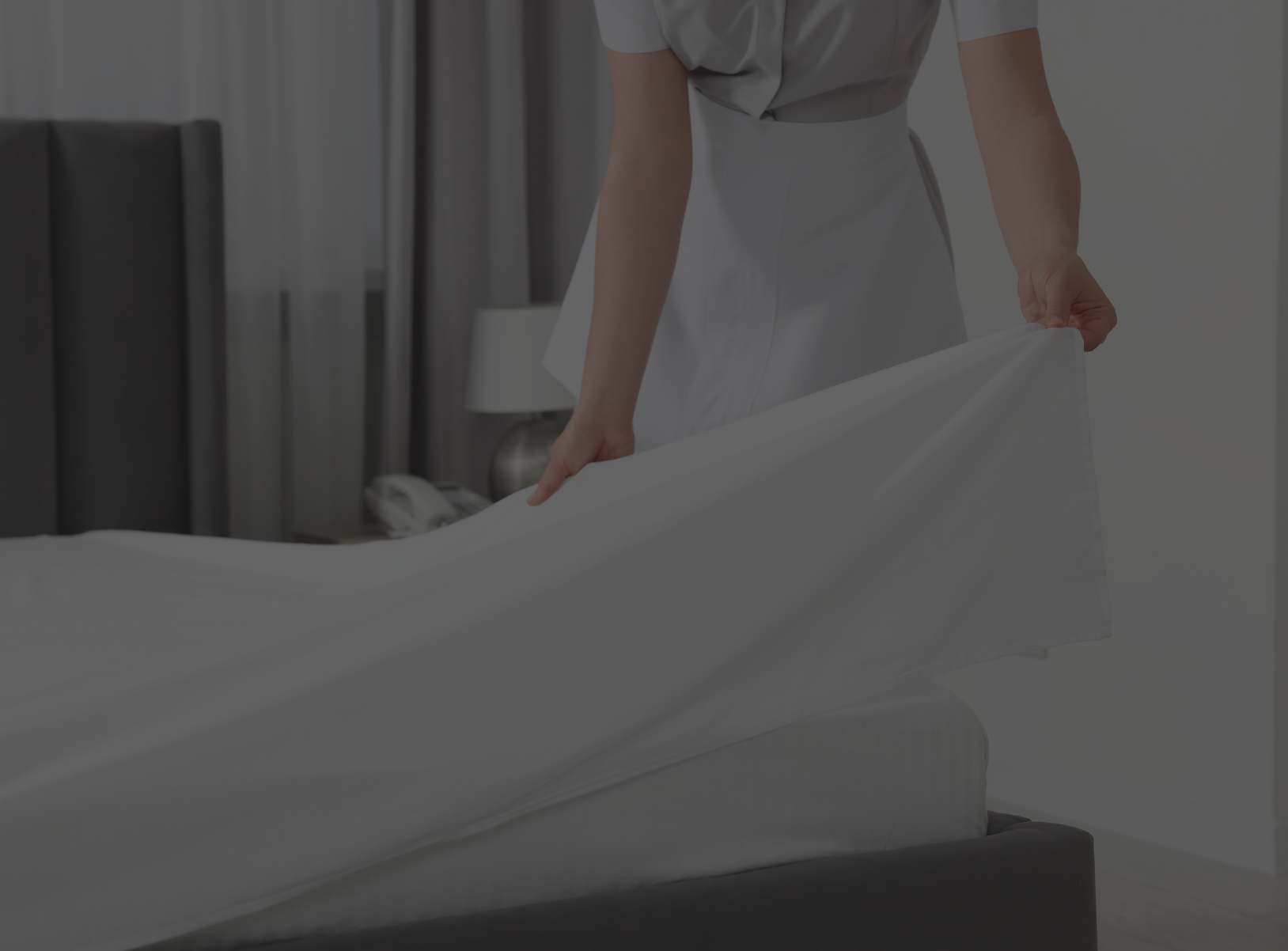 Person making a bed by straightening a white sheet in a bedroom.