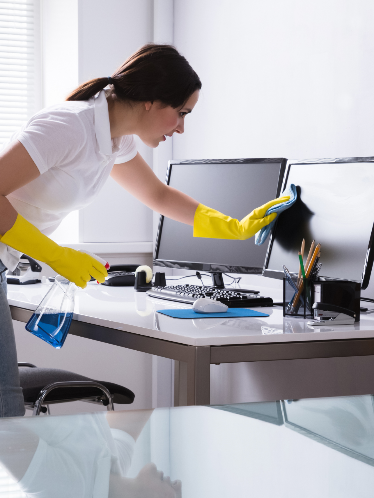 Woman-cleaning-computer-monitor-in-an-office-while-wearing-yellow-rubber-gloves-and-holding-a-spra-bottle.