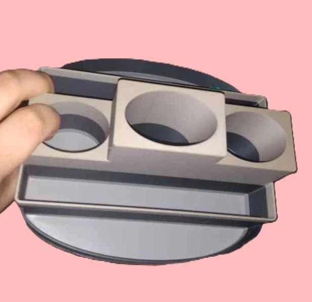 Person holding a three-cup holder over a round, gray tray on a pink background.