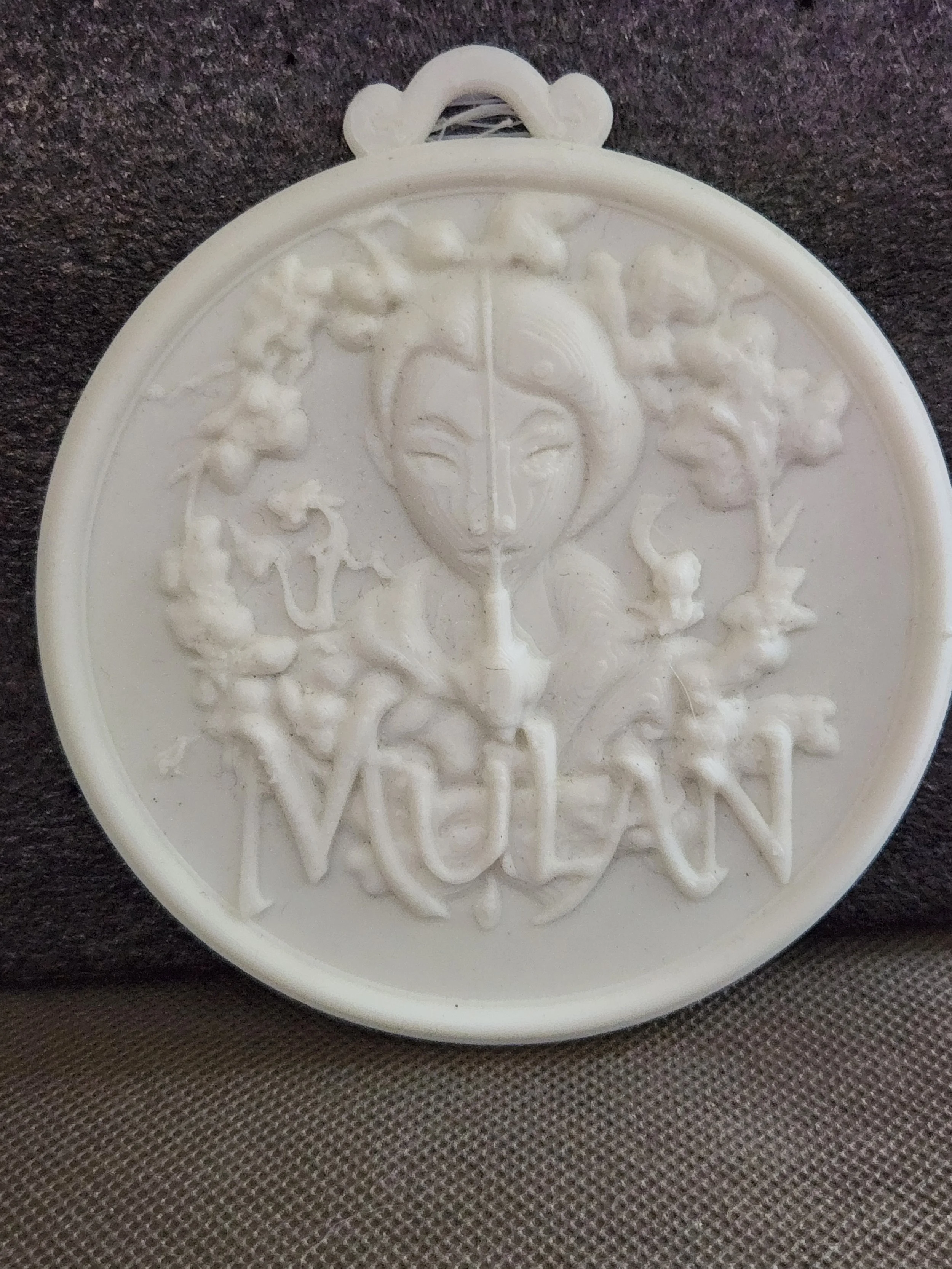 White oval-shaped medallion with an embossed squirrel design, surrounded by tree branches and leaves, on a dark fabric background.