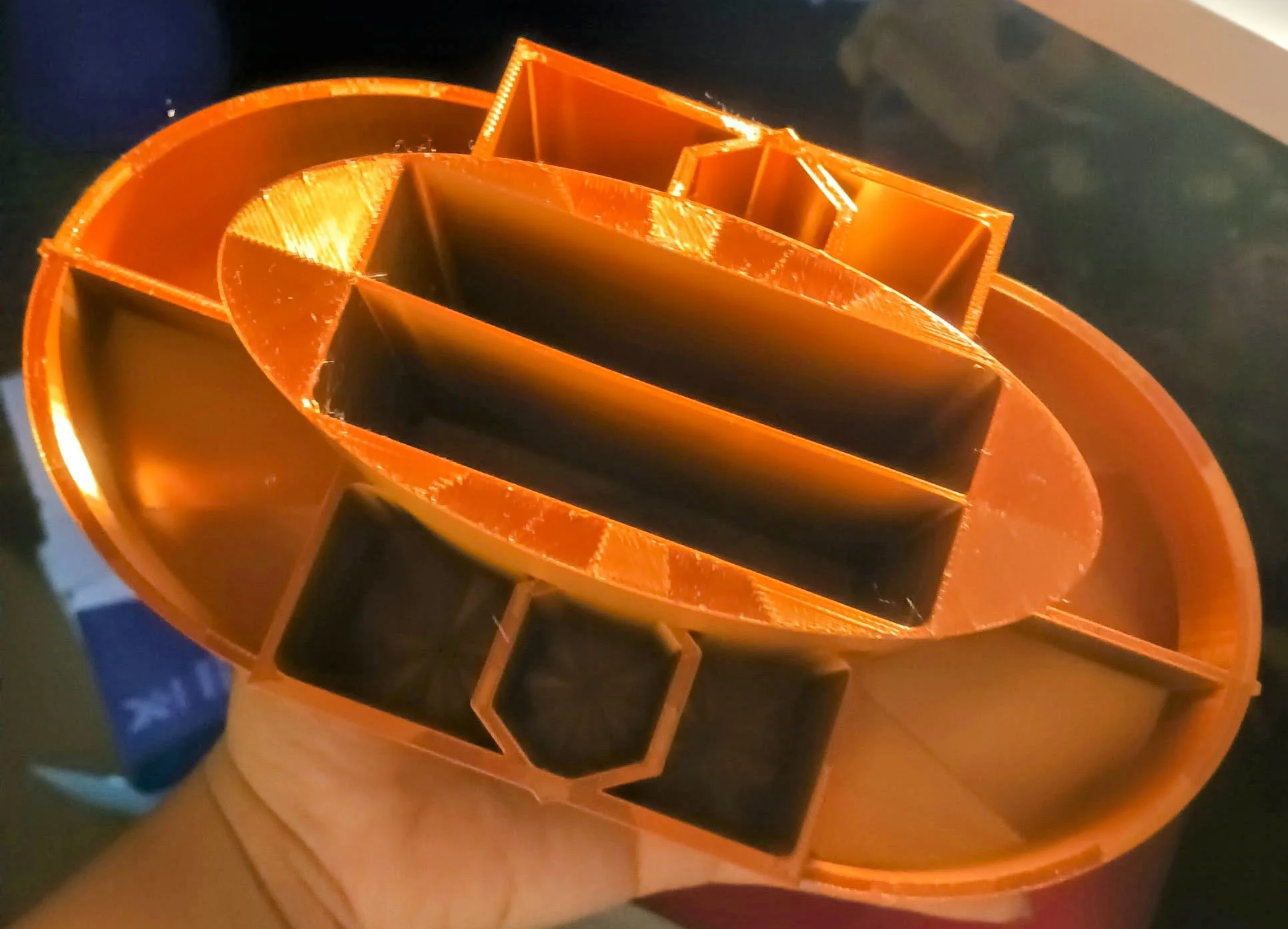 Close-up view of a 3D printed orange pumpkin-shaped cookie cutter with black inserts, placed on a wooden surface.