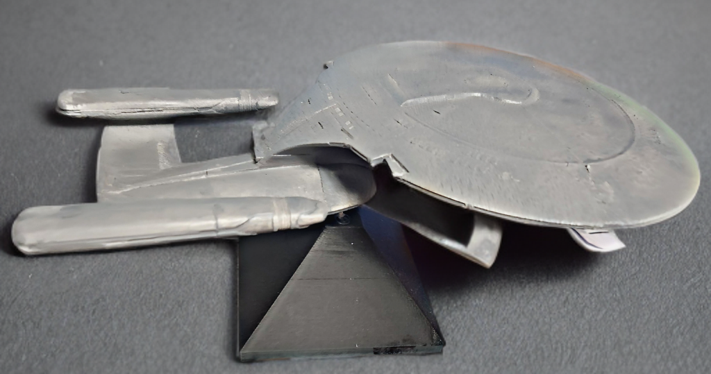 A model of a spacecraft or spaceship made out of metal, displayed on a black stand.