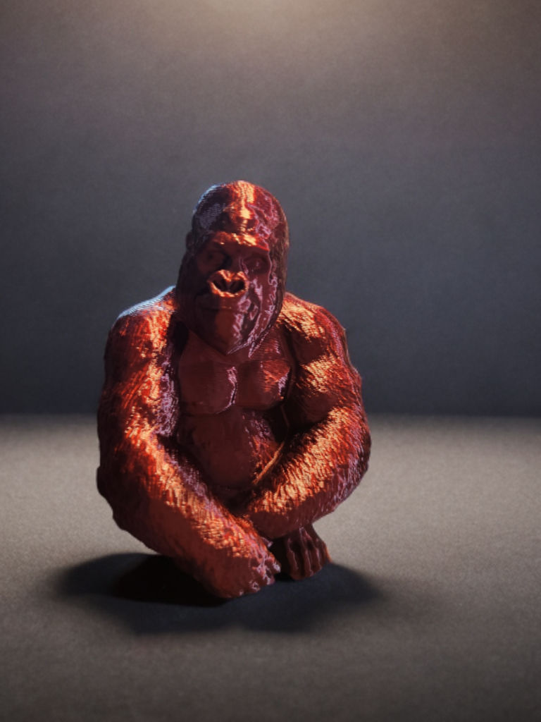 A small sculpture of a humanoid gorilla sitting on a gray surface against a dark background.