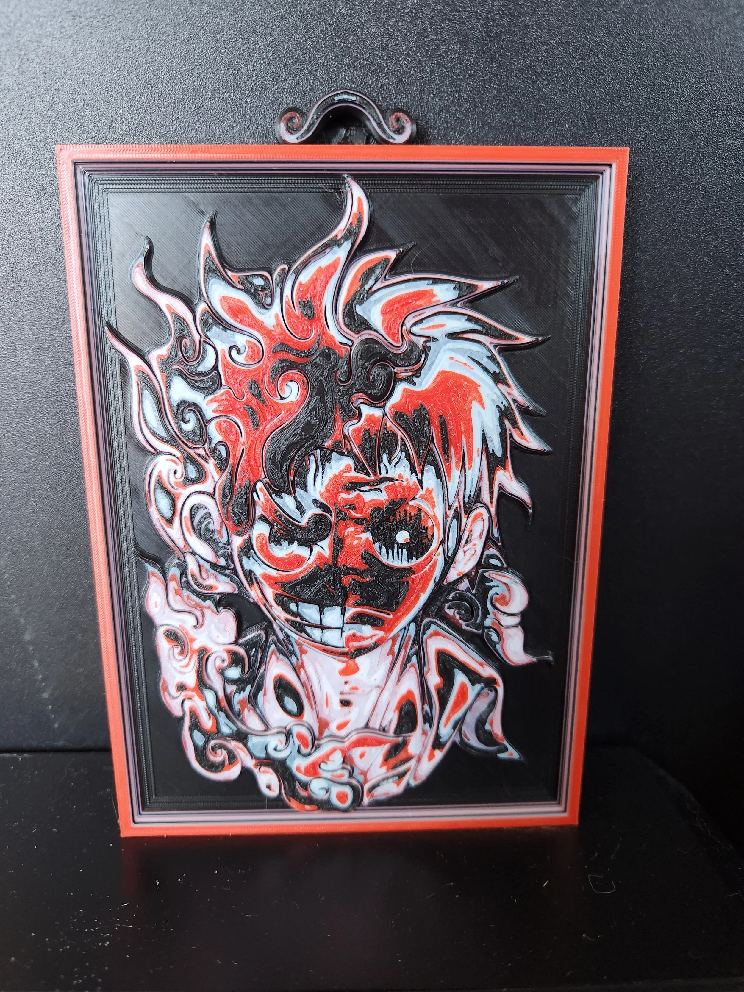 Abstract black, white, red, and blue swirl painting of a dragon on a rectangular canvas with a red border, placed on a black surface.