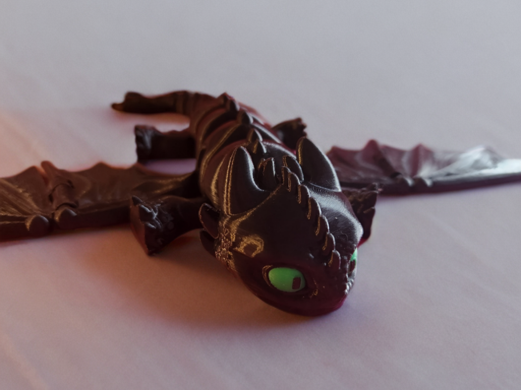 Toy figurine of a black dragon with green eyes lying on a flat surface.