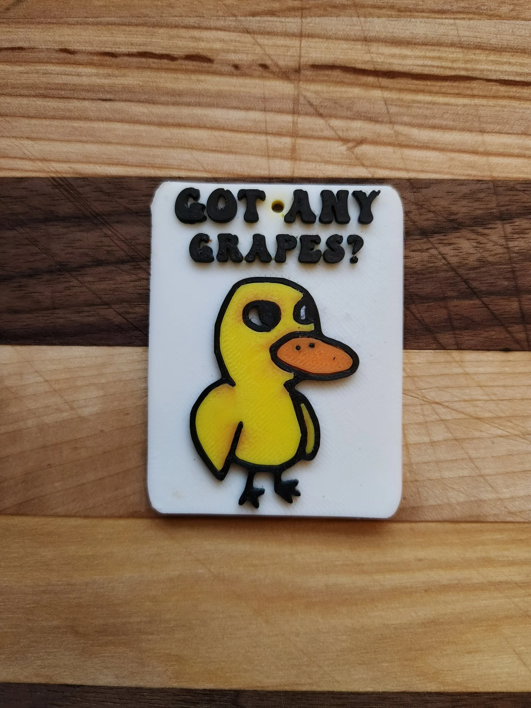 A sticker featuring a cartoon yellow duck with an orange beak, black feet, and black outline, placed on a white background. Text above the duck reads, 'GOT ANY GRAPES?'