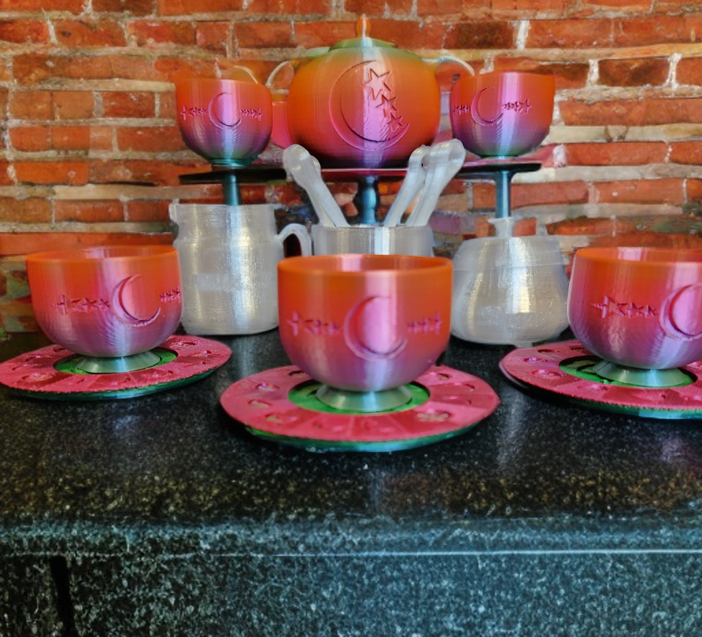 Set of six 3d printed cups with a pink and orange gradient and moon and star designs, each on a matching circular coaster, on a black countertop against a red brick wall, with a teapot, cups, and utensils in the background.